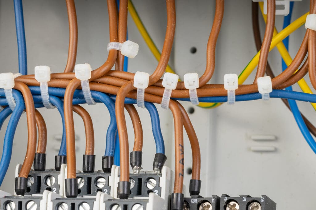 White heavy duty cable ties hold together thick yellow, blue, and orange wires on an electrical control panel.